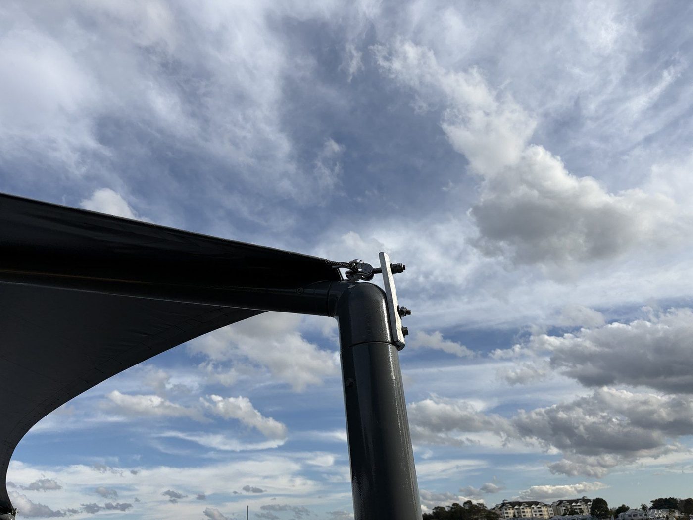 A black shade sail corner tensioned to the head of a steel post against a cloudy sky., Abbotsford
