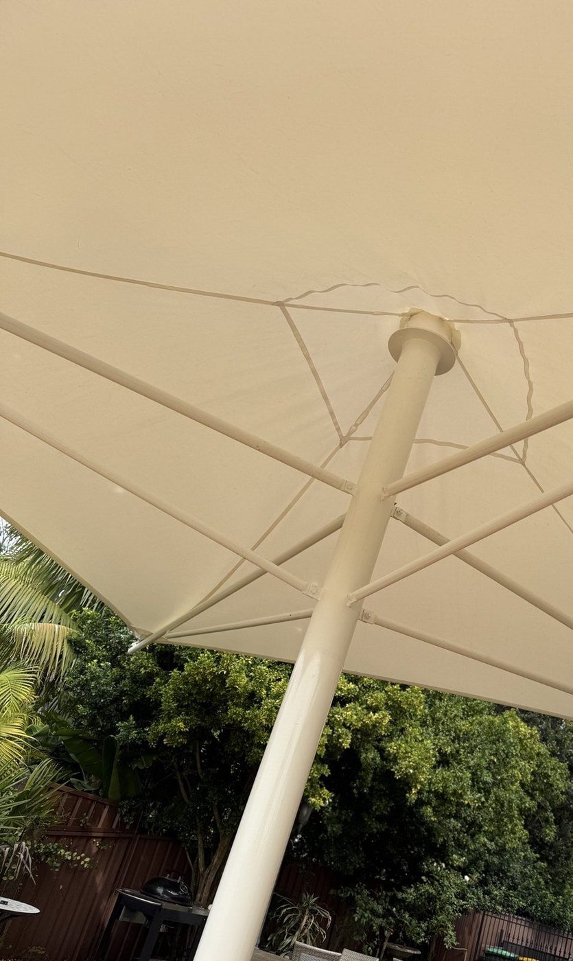 Cream umbrella canopy seen from below, its ribs and centre pole above a leafy backyard patio., Alfords Point