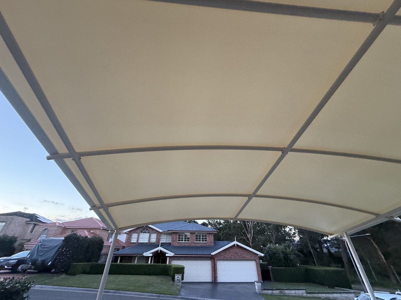 A cream curved canopy on slim white posts over a driveway, seen from underneath at dusk., Beaumont Hills
