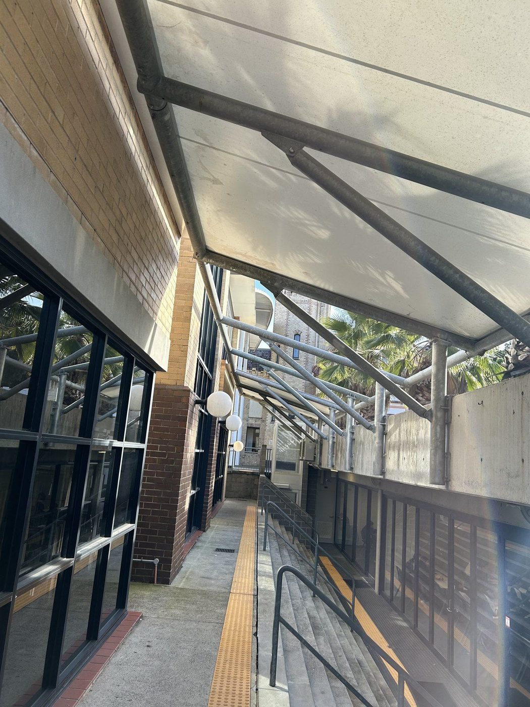 A white fabric canopy on a steel frame covering a walkway and stairs beside a brick building., Belmore
