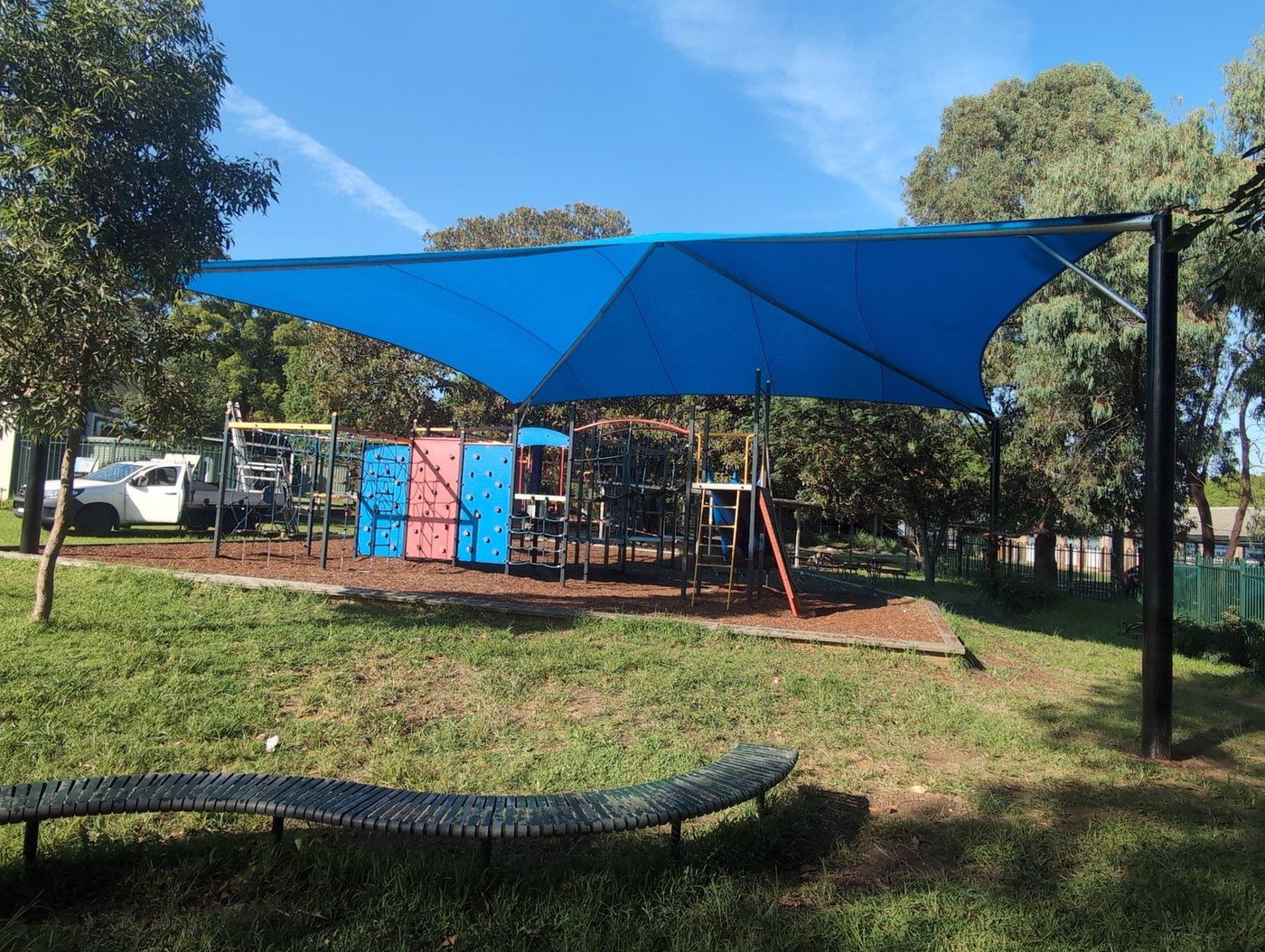 Blue shade canopy on black steel posts covering climbing frames and slides on mulch., Botany