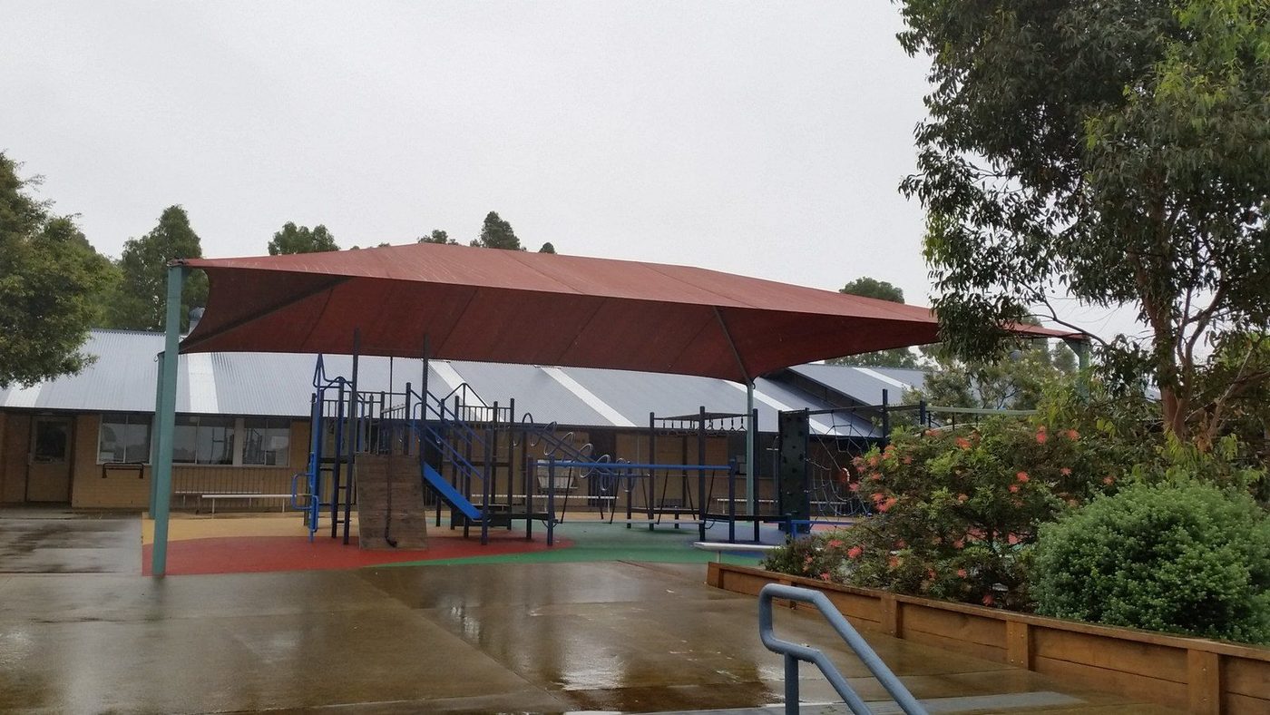 A terracotta shade canopy on steel posts covers playground equipment on a wet day., Botany