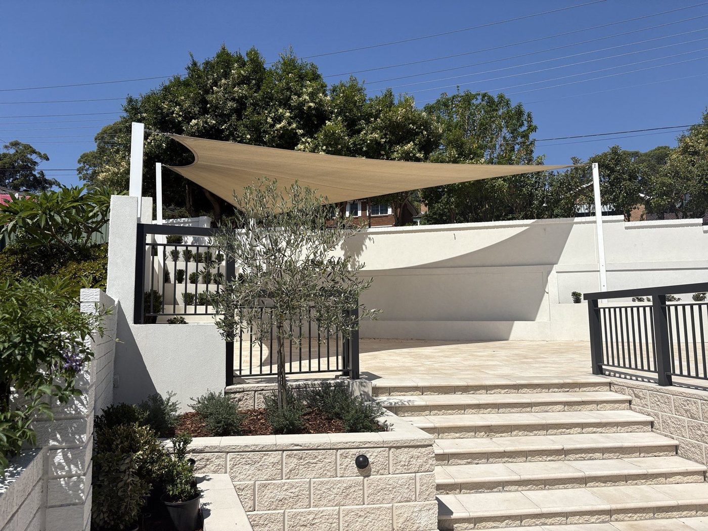 Sand-coloured triangular shade sail over a paved courtyard beside rendered walls and steps., Carlingford
