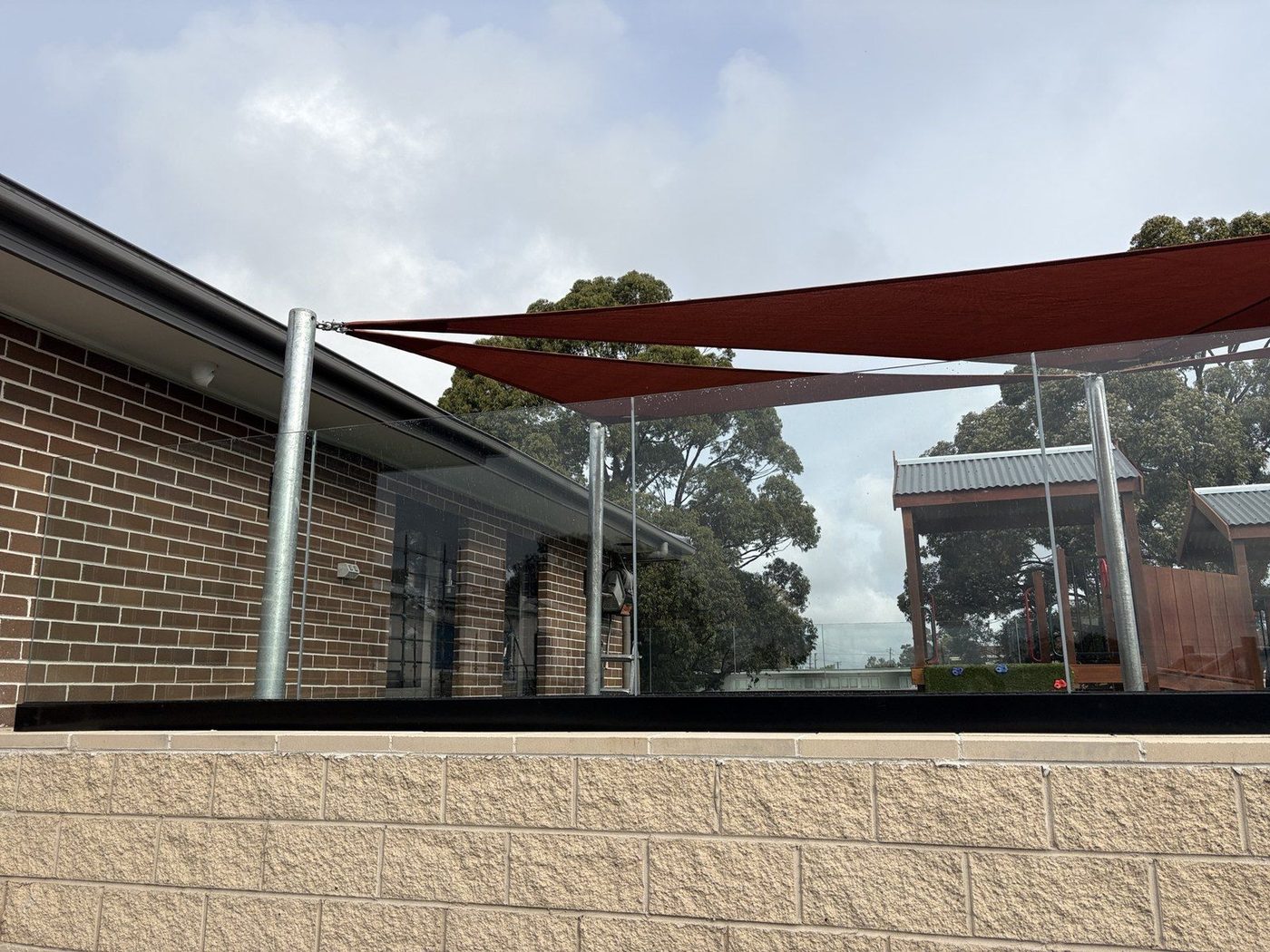 Terracotta shade sails on galvanised posts above a raised paved terrace beside a brick building., Chipping Norton