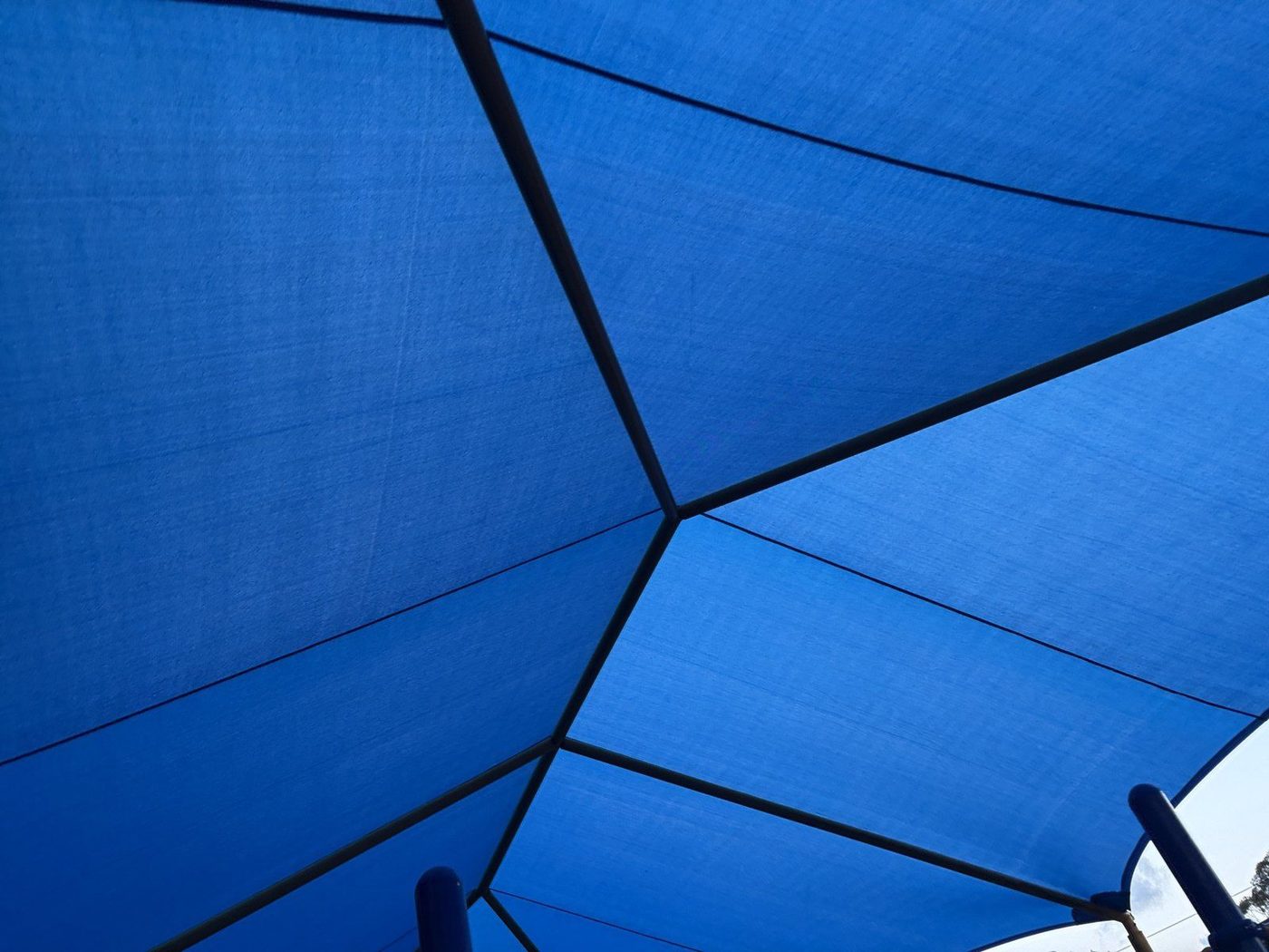 Blue shade sails seen from below against the sky, above a padded playground post., Glenorie