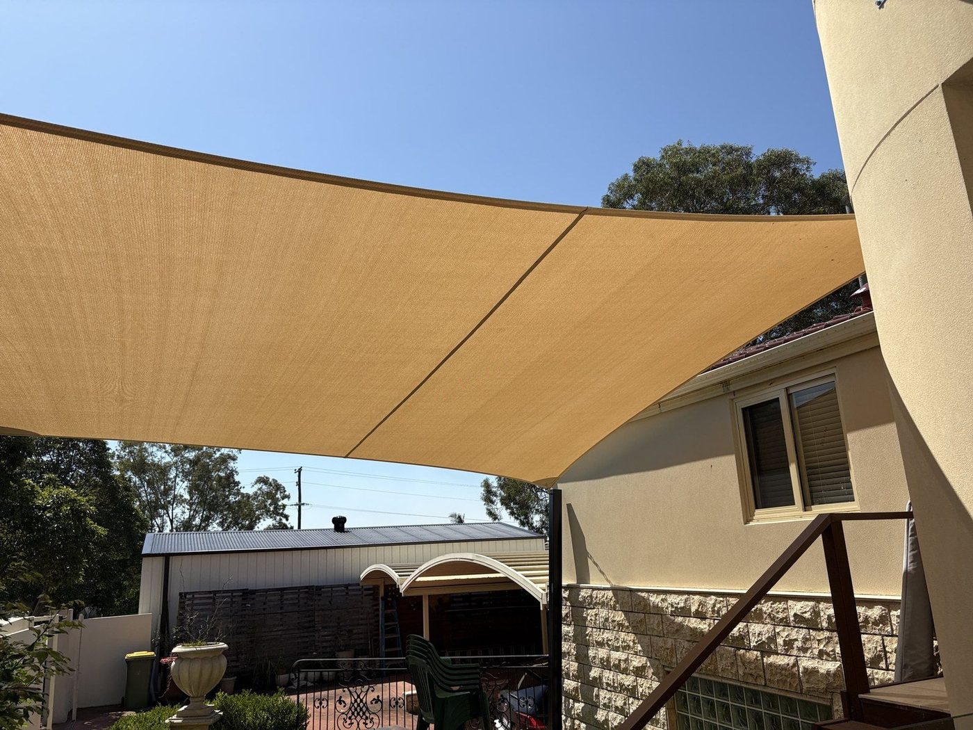 Two sand shade sails angled over a paved backyard beside a rendered two storey home., Greenacre