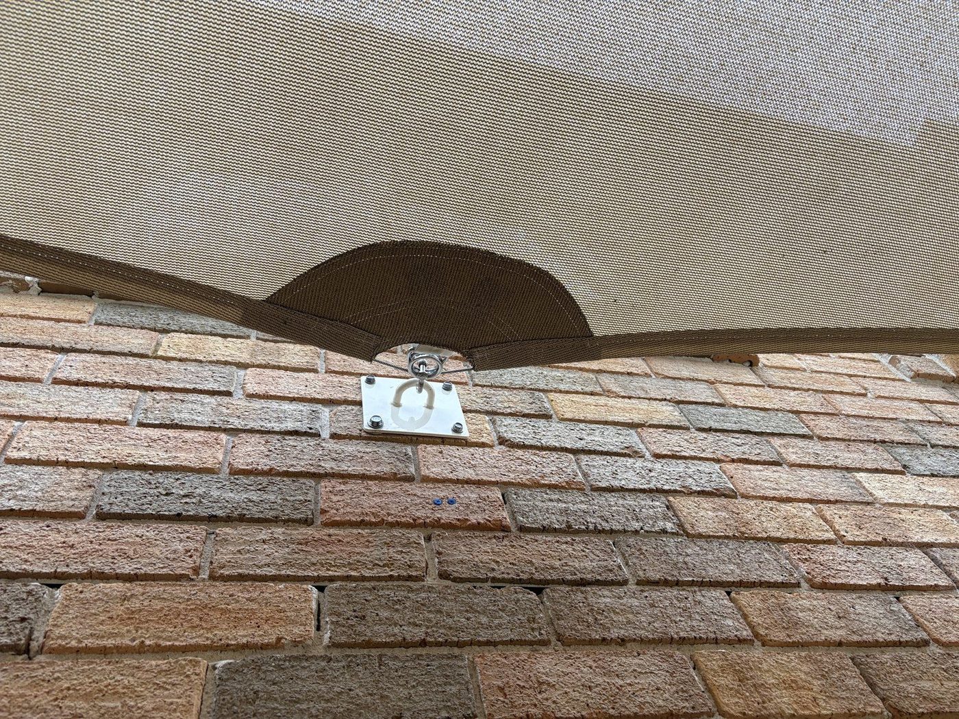 Sand coloured shade sail corner tensioned by a stainless plate and shackle on a brick wall., Kellyville