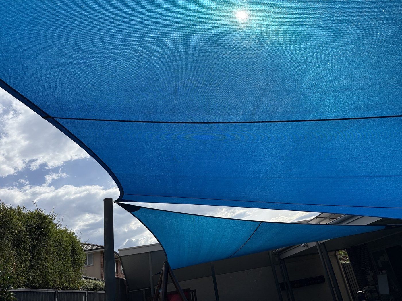 Two overlapping blue shade sails seen from below against a bright sky over a fenced yard., Kellyville