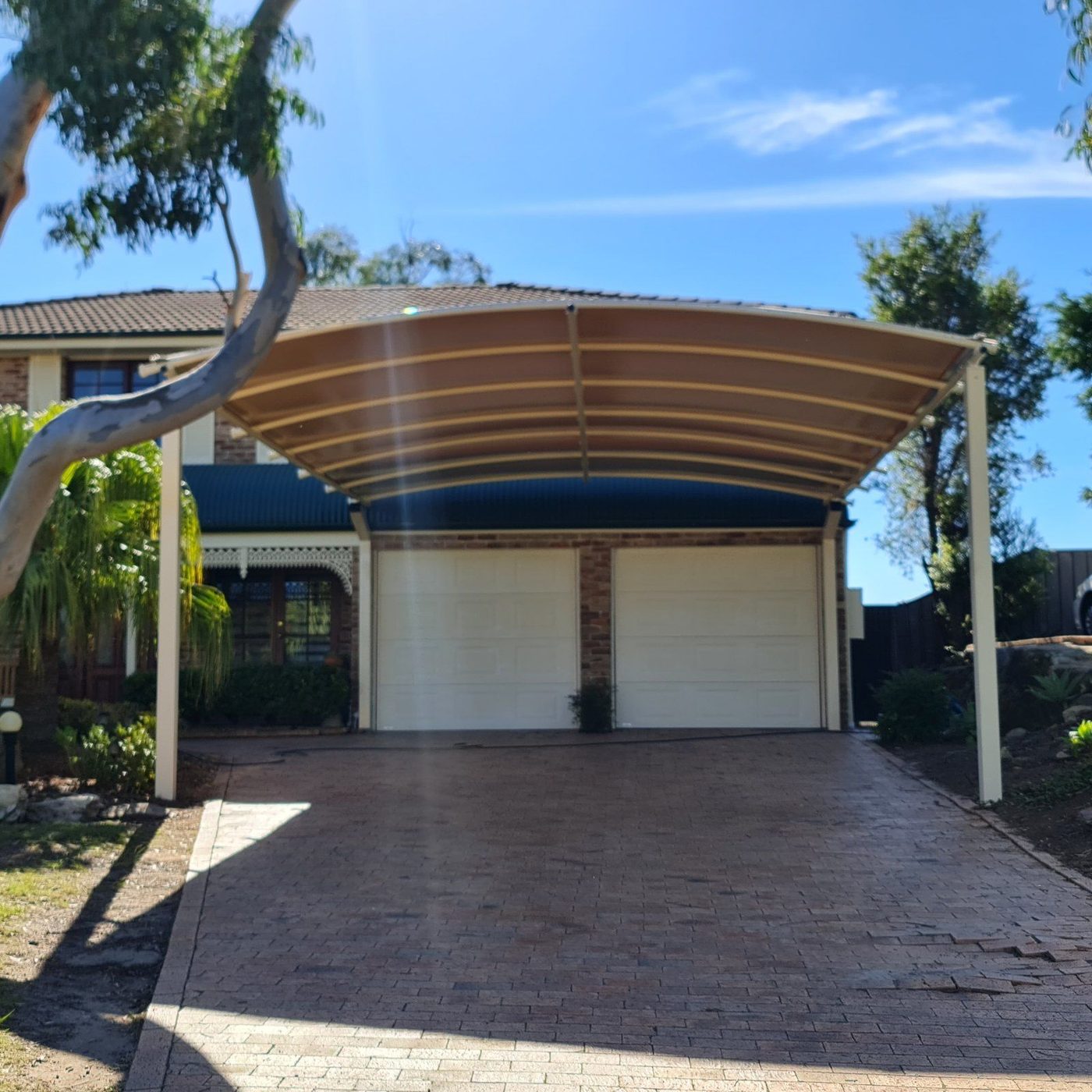 Curved cream carport roof spanning a brick-paved driveway in front of a double garage., Kellyville