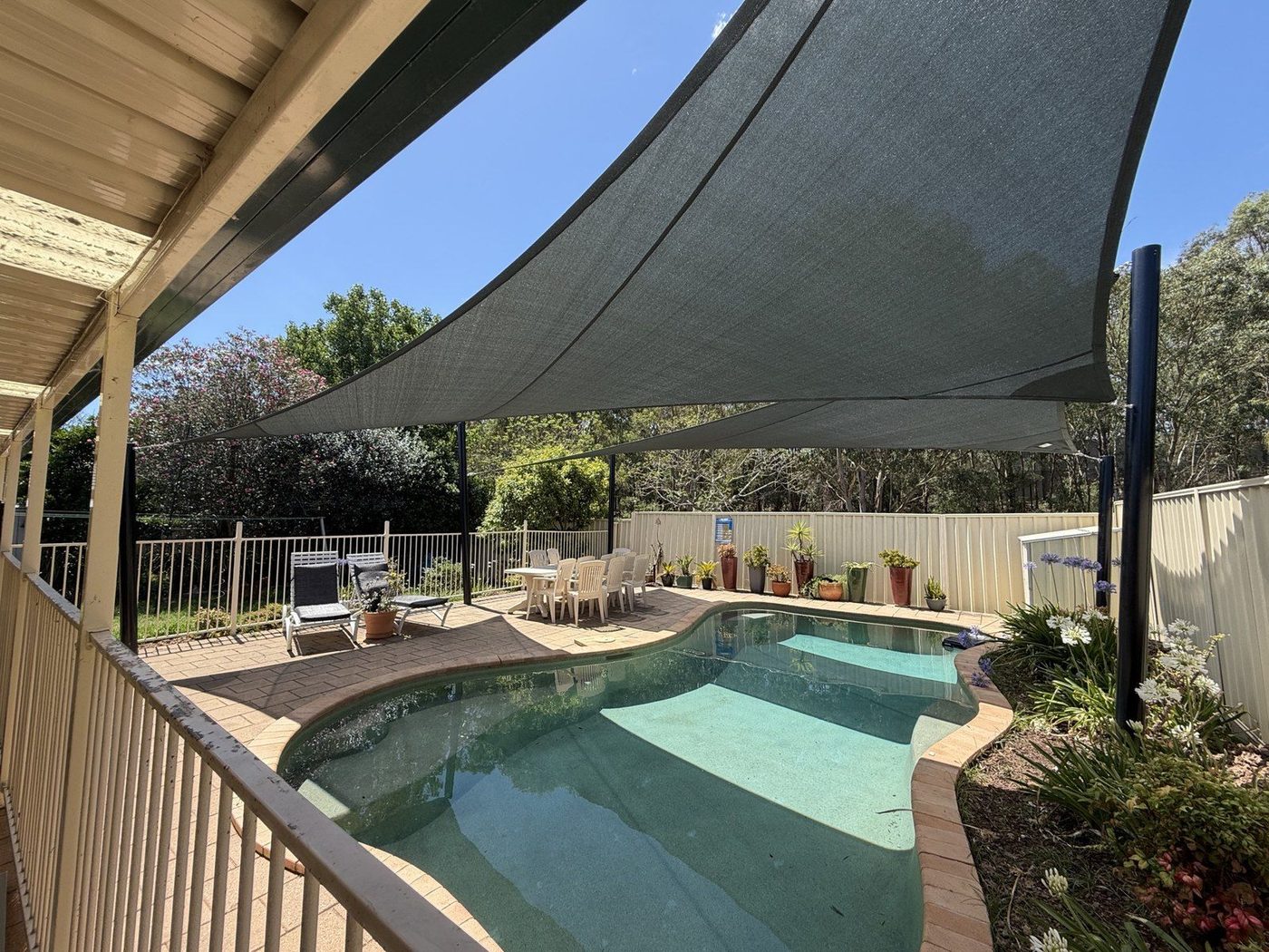 Two charcoal shade sails sweep above a backyard pool beside a home's veranda., Kings Park