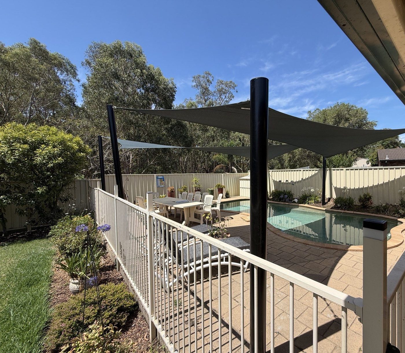 Dark grey shade sails on black posts above a fenced backyard pool and paved area., Kings Park