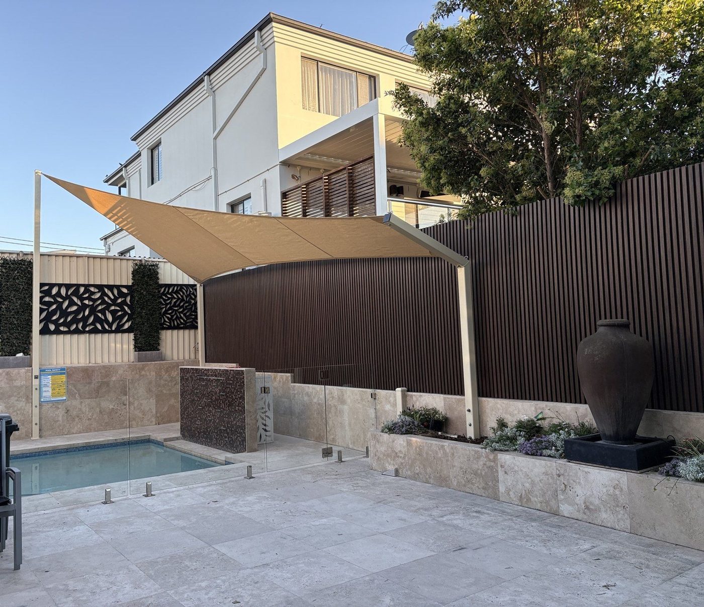 A sand-coloured shade sail on slim posts above a small courtyard pool with travertine paving., Malabar