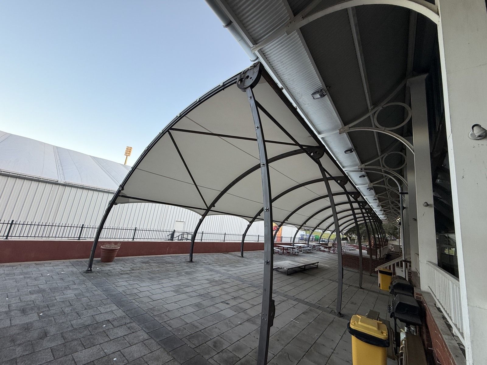 Cream fabric canopy on dark curved steel ribs beside a paved courtyard.