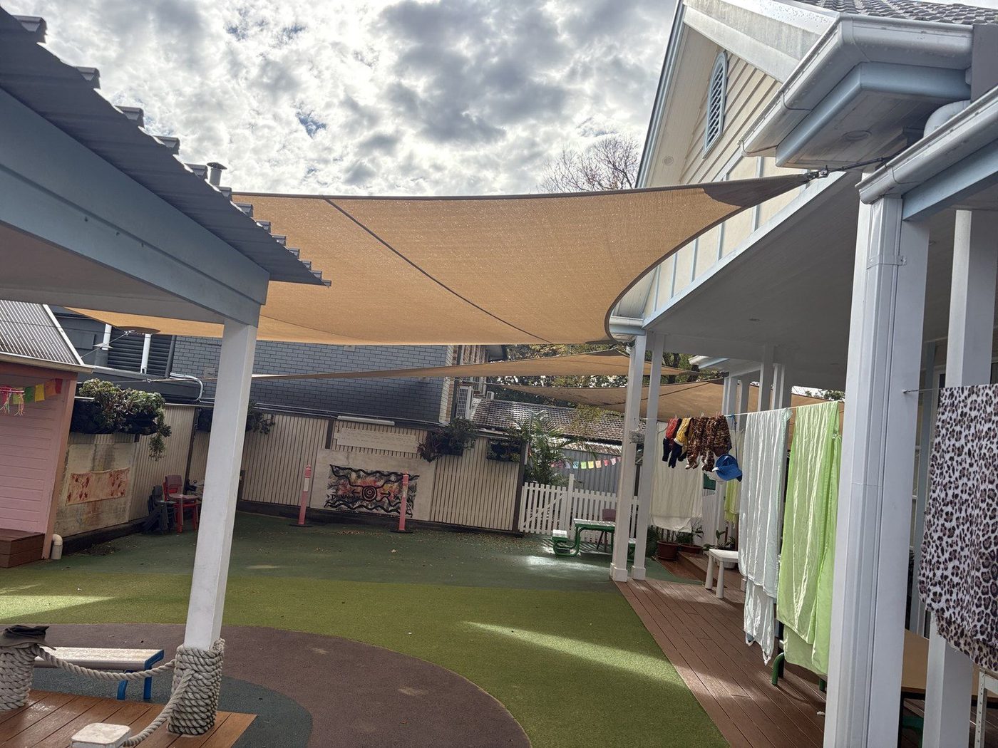 Two sand shade sails over a green synthetic turf play yard with a timber deck and washing line., Narrabeen
