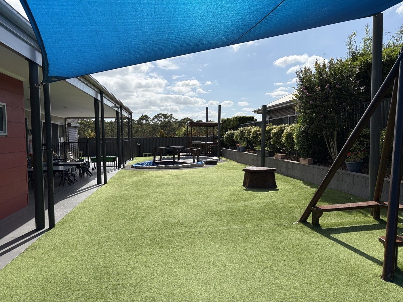 A large blue shade sail stretches over an artificial-turf playground with climbing frames., North Kellyville