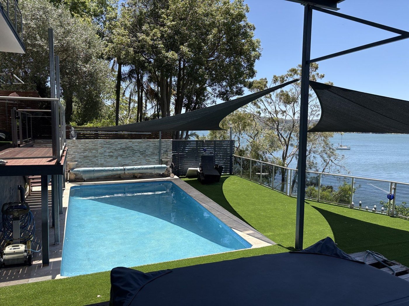Charcoal shade sails above a waterfront pool, with a moored yacht on the water beyond., Point Clare