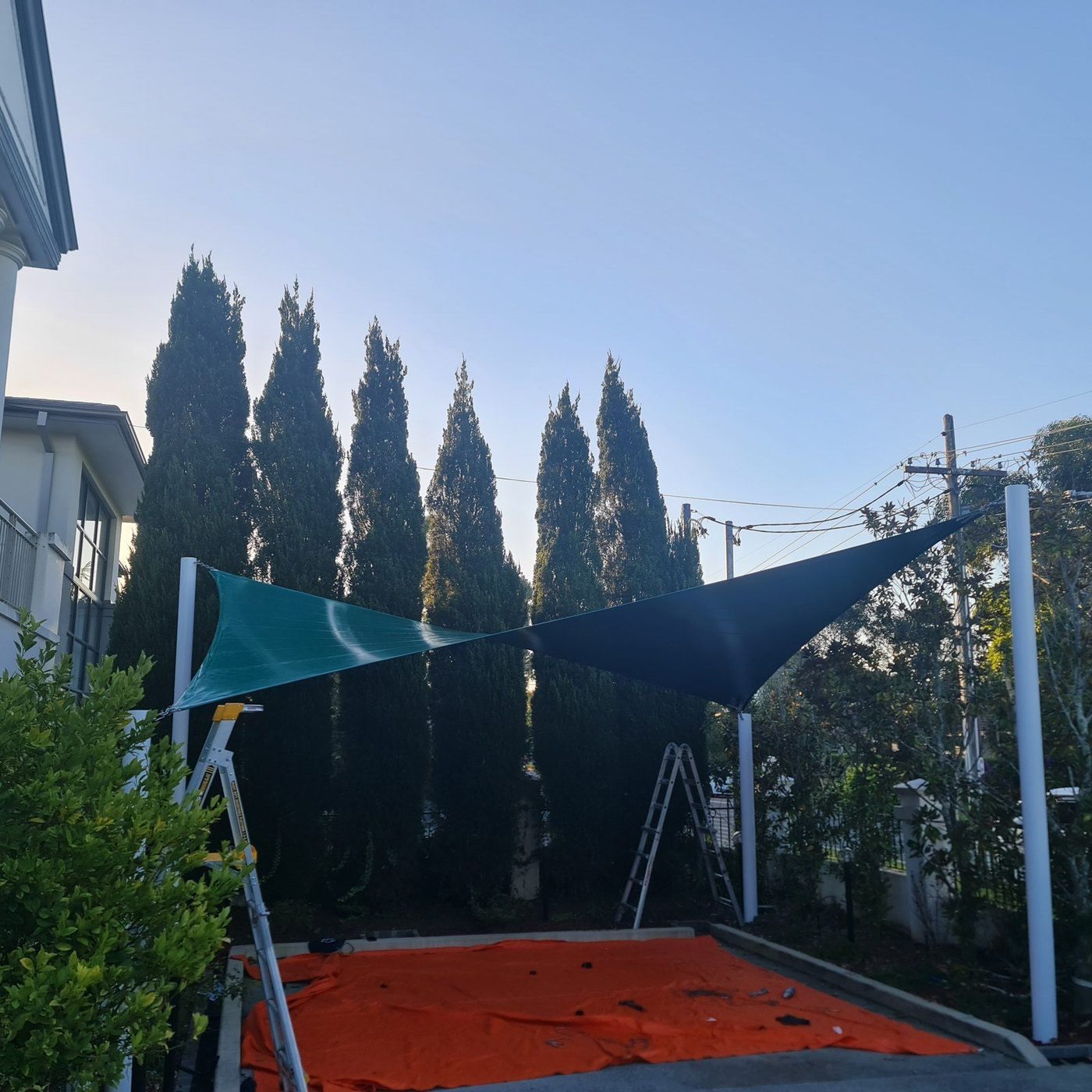 Green and charcoal shade sails on white posts above a paved home yard, with ladders still in place., Port Kembla