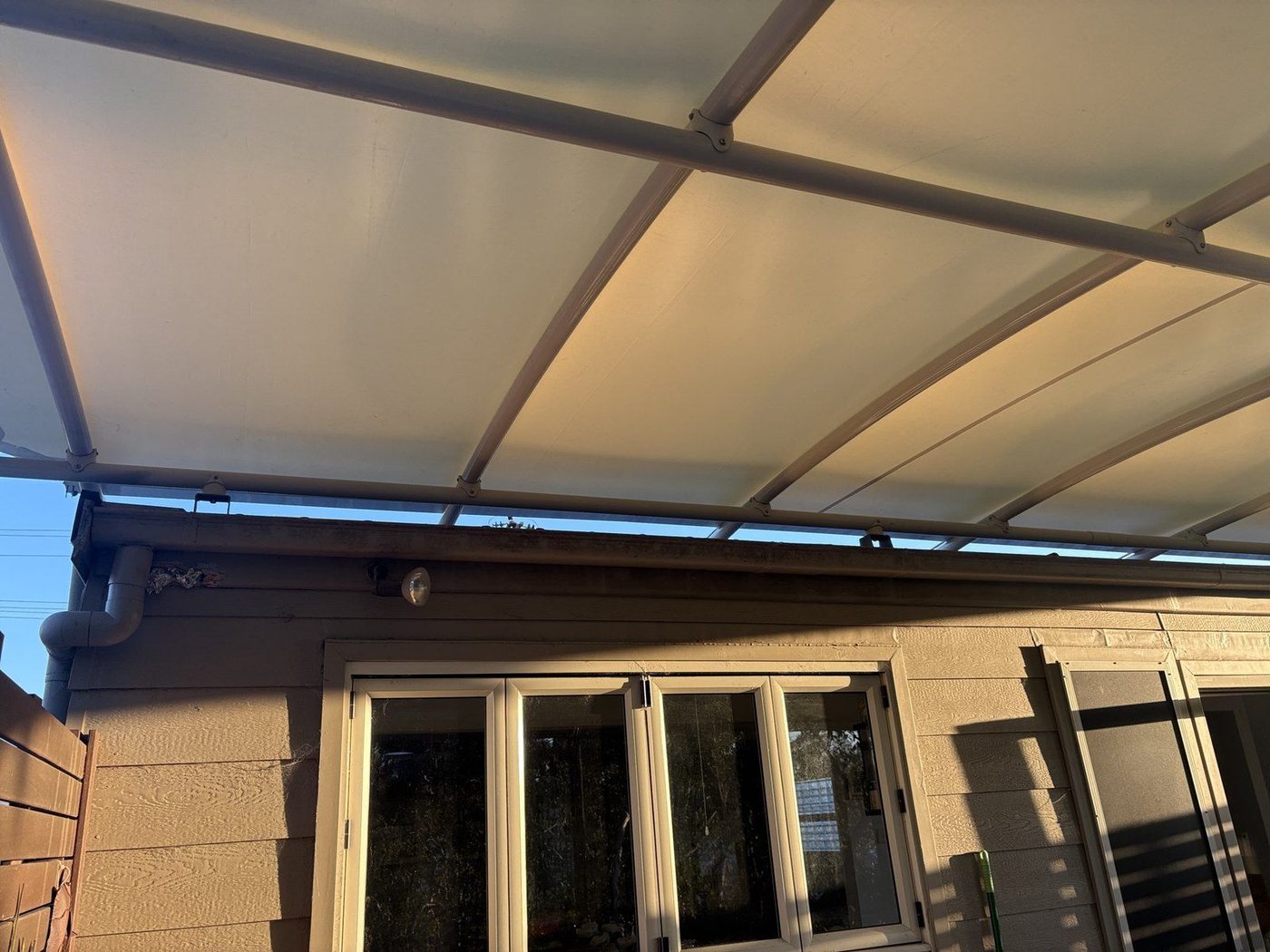A cream canopy on curved rafters shelters a patio outside bifold glass doors at sunset., Tanilba Bay