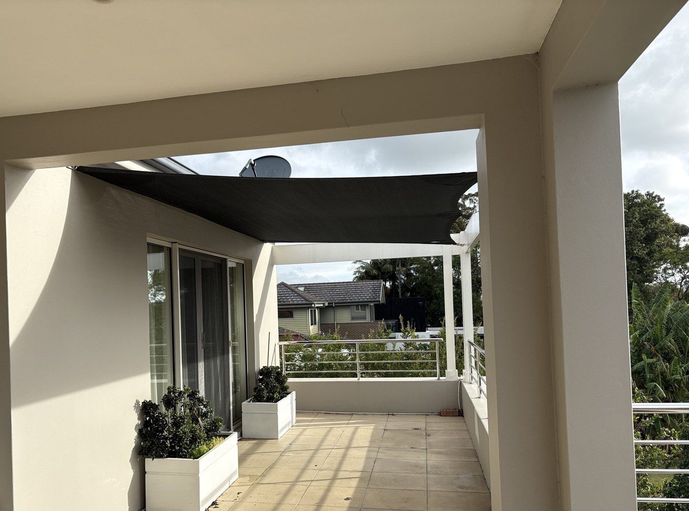 A charcoal shade sail over a tiled balcony with white planter boxes against a rendered wall., Tennyson Point