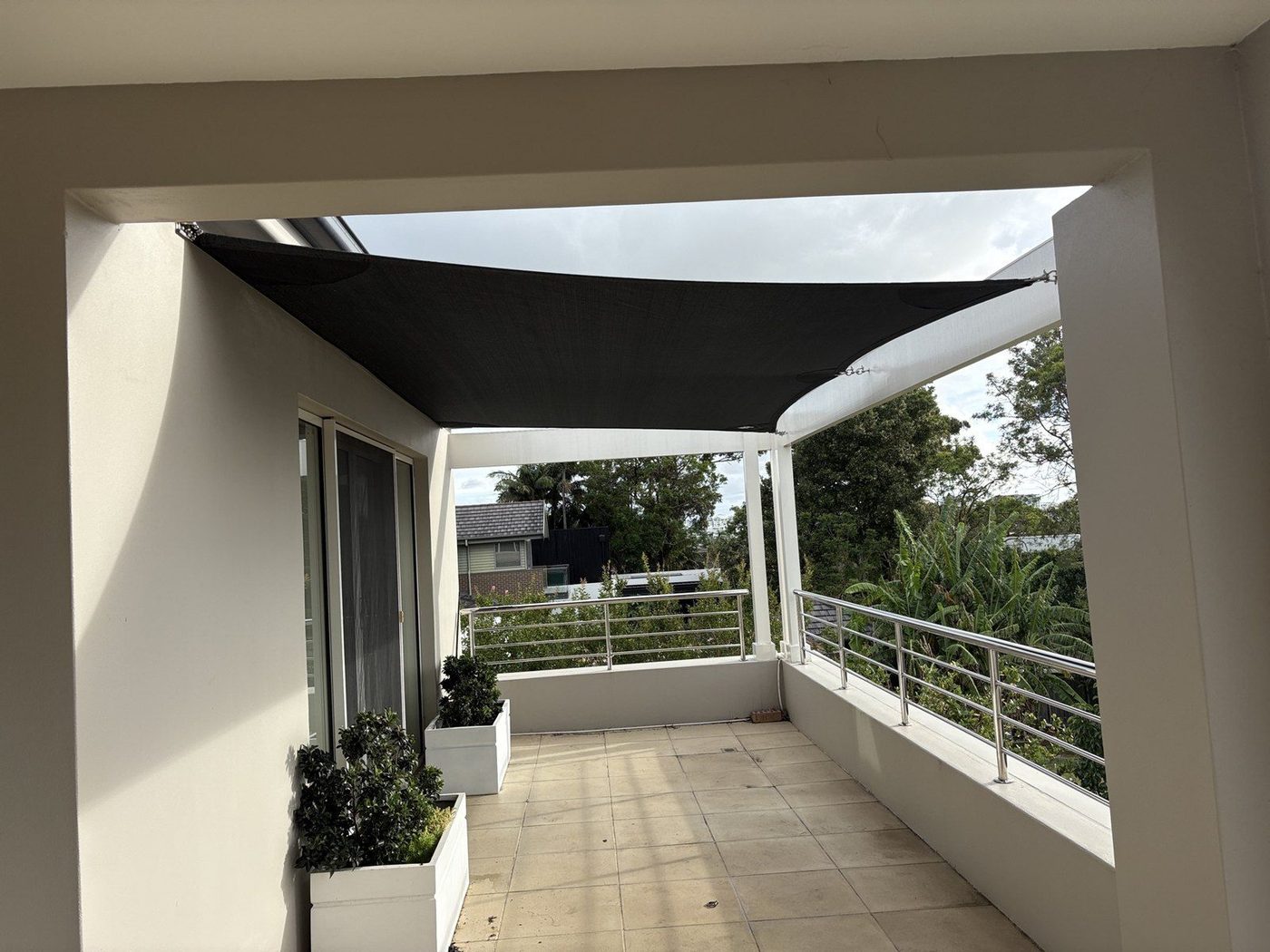 A charcoal shade sail tensioned across a tiled residential balcony with planter boxes and a steel rail., Tennyson Point