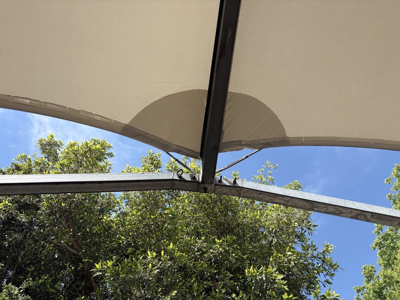 Cream canopy seen from below, carried on curved galvanised steel beams against a blue sky., Wareemba