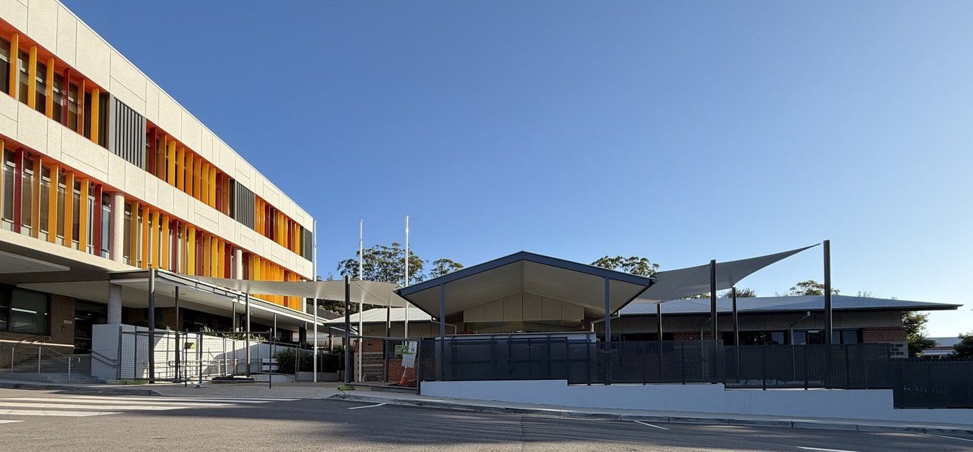 White shade sails and a metal-roofed shelter along a school walkway under a clear sky., West Gosford