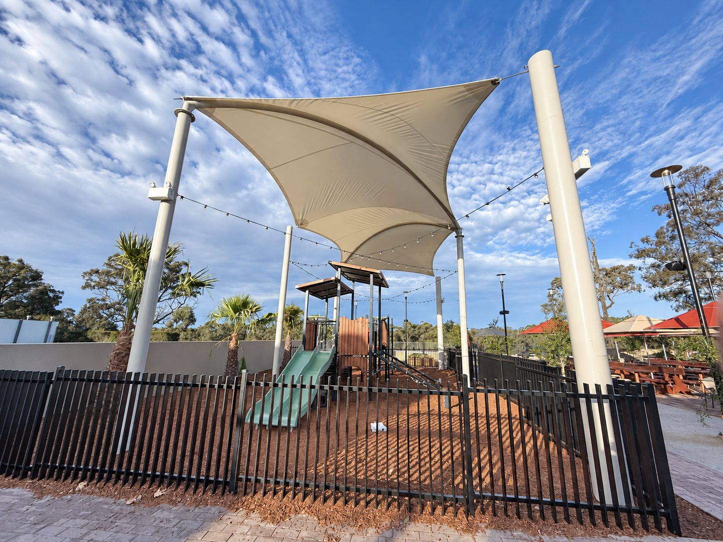 Cream fabric canopies on tall pale posts above an empty fenced play area.